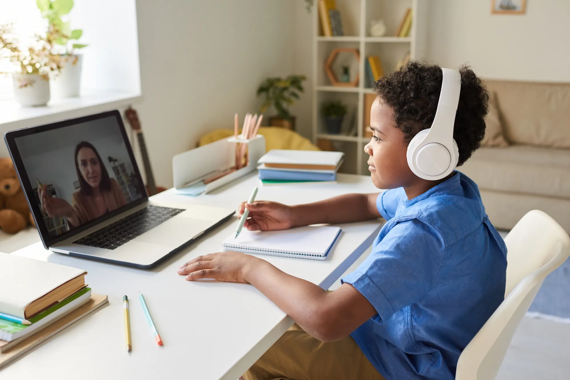 Boy wearing headphones writing notes during a video lesson