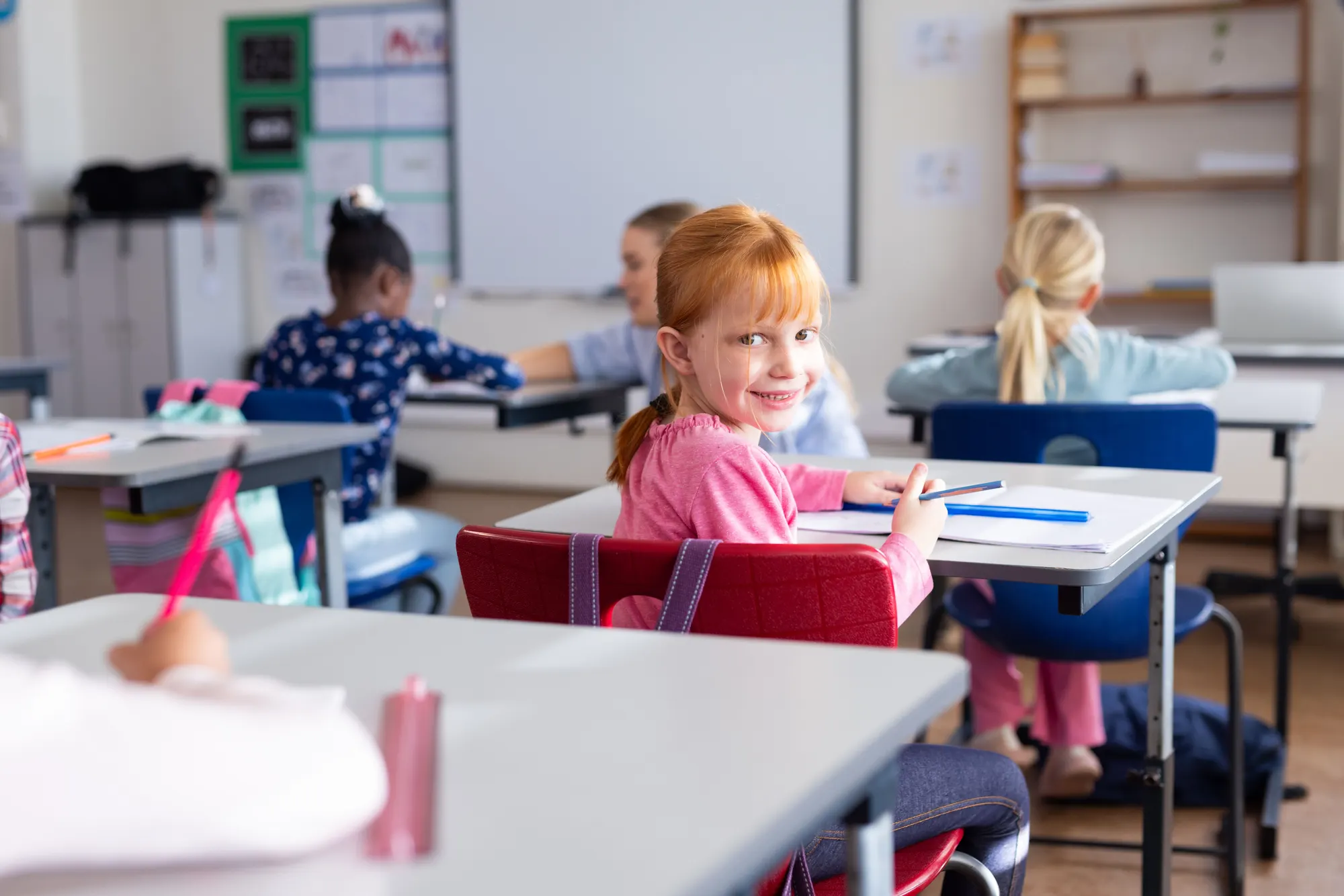 Girl in a classroom turning round from her desk to smile