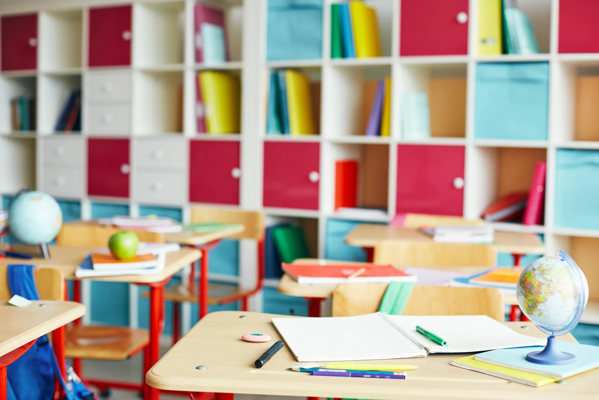 Bright classroom with desks, books, an apple and a globe
